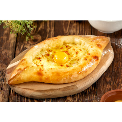 Chatschapuri Adscharuli - Khachapuri aus Ajara wird der Teig zu einer offenen Gondelform geformt und vor dem Servieren mit einem rohen Ei und Butter belegt wird.